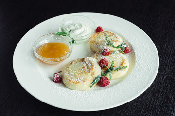 cheese pancakes with raspberries and honey on a white plate on a wooden table