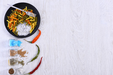 Obraz na płótnie Canvas plate with pasta, fork, spices in jars, chili pepper