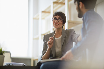 Two cheerful colleagues smiling while discussing something in modern office, focus on stylish...