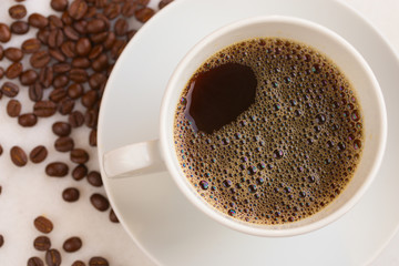 White cup of coffee with coffee beans are scattered around.