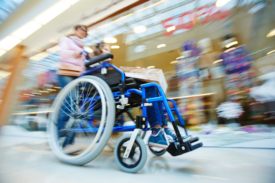 Woman pushing wheelchair with her daughter in the mall