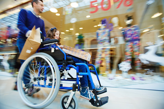 Man pushing wheelchair with daughter in shopping-center