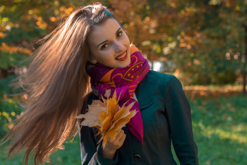 attractive young girl with long hair in a pink scarf keeps its leaves in his hand and smiles