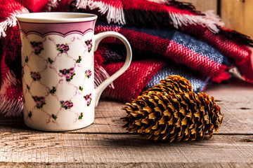 Cup of tea and warm plaid blanket on wooden rustic bench, picnic in the autumn forest. Fall weekend. Photo toned, selective focus.