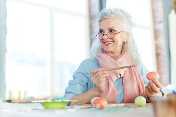 Attractive senior woman painting Easter eggs at home