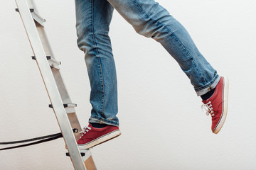 Mann balanciert auf einem Bein auf einer Leiter, Unfallgefahr, untere Körperhälfte