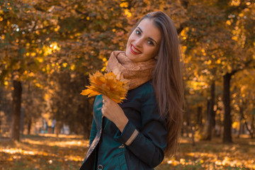 Naklejka na ściany i meble cheerful young girl in the Park keeps the leaves in his hand looks straight and smiling