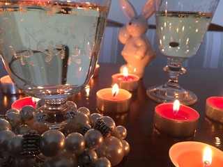 Sekt Gläser mit Perlen schmuck Armband und rosa farbenen brennenden Teelichtern mit weißem Hase vor hellem Hintergrund am Esstisch