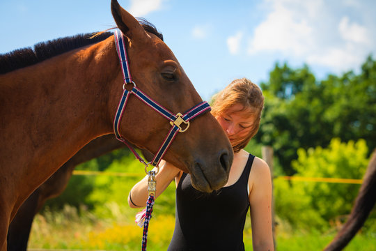 Jockey young girl petting and hugging brown horse