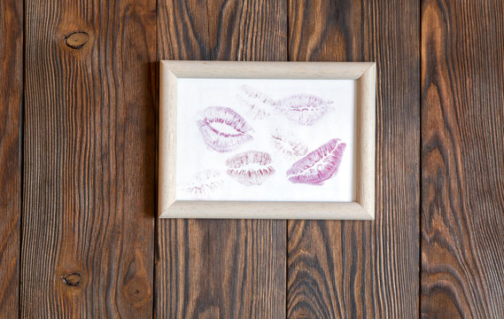traces of lipstick kisses on a white paper in a frame. Dark wood