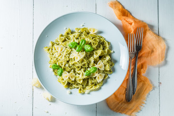 Healthy pasta with green pesto and basil on white table