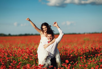 Naklejka na ściany i meble happy couple having fun in a field of poppies