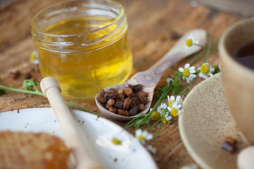 Serving table: drawn honey comb with honey dipper on a ceramic plate with cup of black tea.