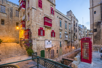 Valletta, Malta - Red vintage british telephone box and footbridge and traditional red balconies in the ancient city of Valletta early in the morning