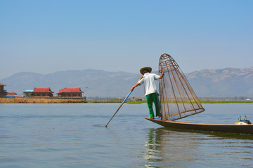 Burmese Fisherman on a boat catching fish by a handmade net in Inle Lake, Myanmar.