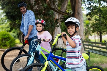 Father and children standing with bicycle in park
