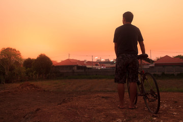 Man stand near bicycle and looking the sunset.