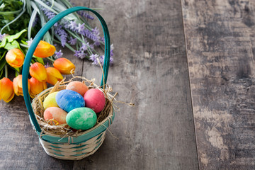 Easter eggs in a basket and tulips on wooden background
