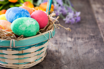 Easter eggs in a basket and tulips on wooden background
