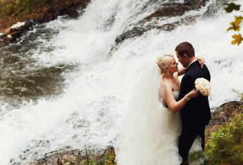 Beautiful stylish newlyweds posing near the waterfall outside