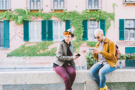 Two young caucaisan man and woma outdoor in the city using smart phone hand hold, talking and smiling - technology, social network, freindship concept