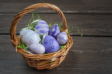 Easter wicker basket with colored eggs on grey wooden board.