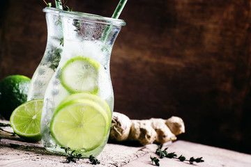 Ginger ale with lime, thyme and ice, vintage wooden background,