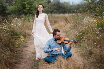 Naklejka na ściany i meble Violinist and woman in white dress , young man plays on the violin the background nature,Young hipster musician man playing violin in the nature outdoor lifestyle