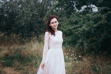 Fototapeta na wymiar Wedding. Young beautiful bride with hairstyle and makeup posing in white dress.Soft sunset light summer portrait. Girl looking in camera