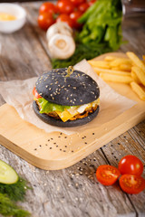 Black hamburger with bacon and sauce on a wooden stand