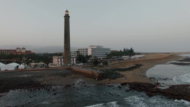 Flying from the coast with resort and lighthouse in the evening. Maspalomas, Gran Canaria