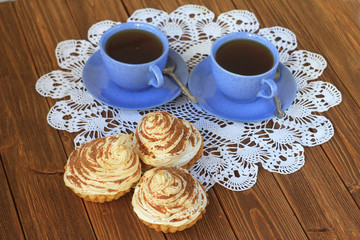  two cups of tea and cakes on a white tablecloth on a dark wooden table