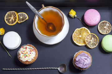 Tea in a cup and saucer, dried yellow roses, cake on a black background.