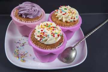 the cupcakes with white and violet cream with spoons on the black background