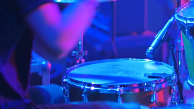 Close-up - the drummer playing on a drums in blue light on a concert