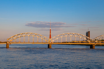 Obraz premium Train is running by the bridge over Daugava. TV tower and sunset time. Riga, Latvia