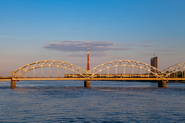 Train is running by the bridge over Daugava. TV tower and sunset time. Riga, Latvia