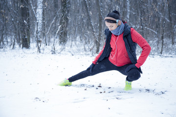 Running sport woman. Female runner jogging in cold winter forest wearing warm sporty running clothing and gloves headphones. Beautiful fit female fitness model.