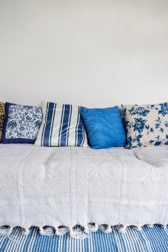 Detail view of white couch with many pillows and blue/white carpet in front. Clean white wall. Interior design concept.