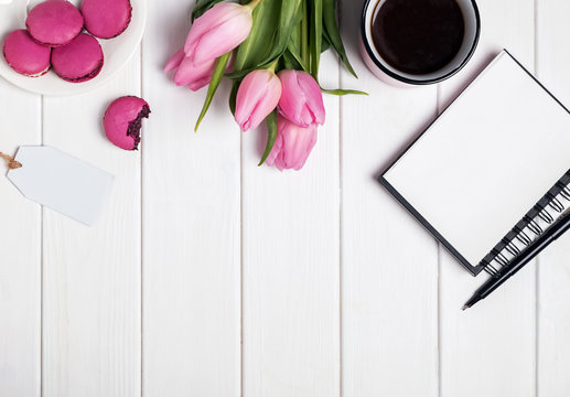 Pink tulips, macarons, empty notepad and coffee on white wooden