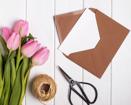 Pink tulips and envelope with blank papr on the white wooden tab