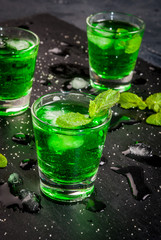 Sweet refreshing mint liqueur, with ice and mint leaves on the slate tray to feed on gray concrete stone table, close view