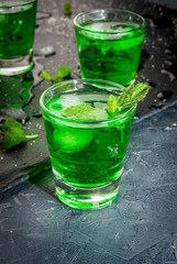 Sweet refreshing mint liqueur, with ice and mint leaves on the slate tray to feed on gray concrete stone table, close view