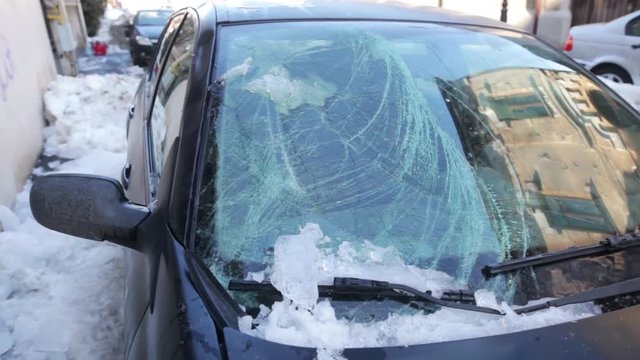 Footage of the broken windshield of a car after a piece of ice has fallen from the roof of a house.