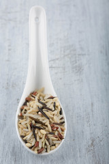 A mix of 4 types of rice in a white ceramic spoon.  Weathered wood background. 