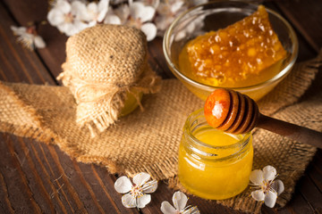 Obraz na płótnie Canvas Honey dripping from a wooden honey dipper in a jar on wooden grey rustic background
