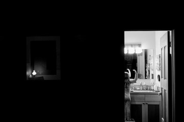 Young girl, standing on stool in bathroom, looking in mirror, black and white