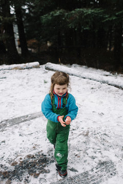 Young girl outdoors, walking in snow, holding snow in hands