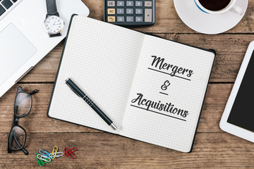 Text "Mergers & Acquisitions" on note book at office desktop