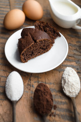 Cake, flour, sugar, cocoa, milk and eggs on a wooden table. Ingredients for cooking.
